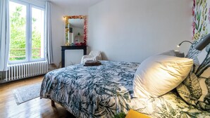 Un dormitorio con una cama grande, una mesita de noche, un espejo y una ventana con cortinas.
