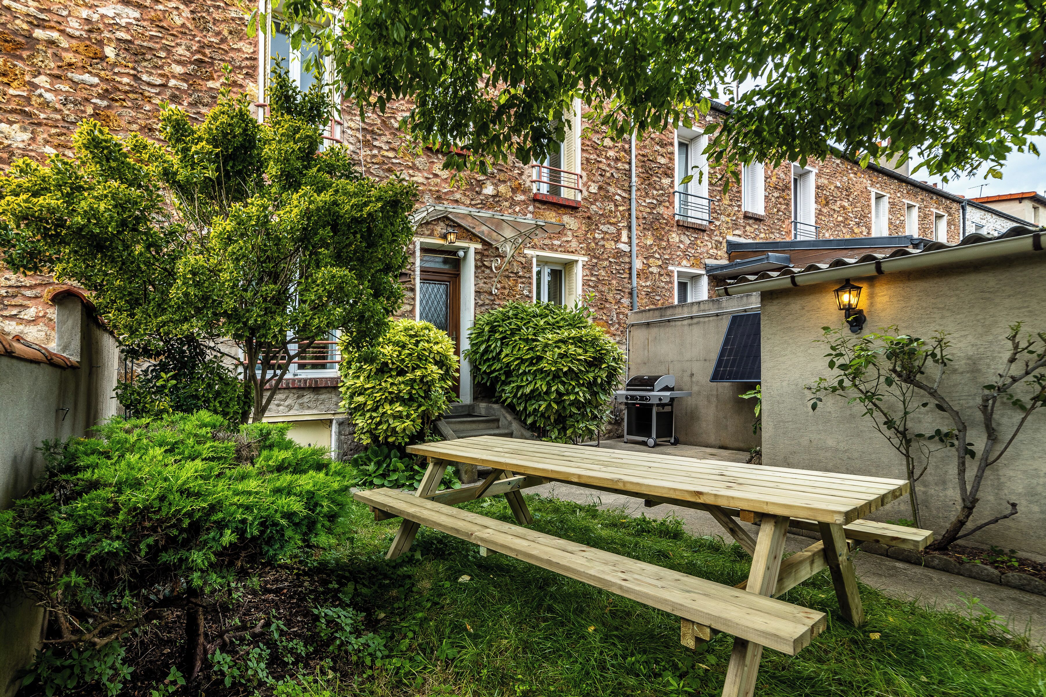 A stone building with a wooden picnic table and a barbecue grill in the yard.