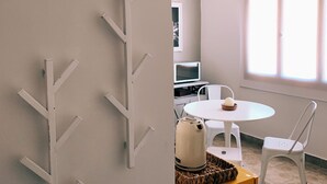 Une pièce avec un porte-manteau blanc fixé au mur, une table ronde avec une chaise, une bouilloire et une petite boîte en bois.