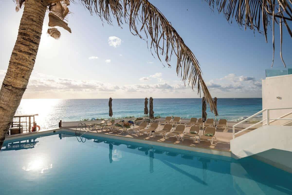 Een zwembadterras met ligbedden en parasols, met uitzicht op een strand en de oceaan.