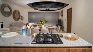 A modern kitchen with a central island, stainless steel appliances, and a dining area with a table and chairs. - Modern retreat with Rooftop Pool + Work Lounge (Cancún)