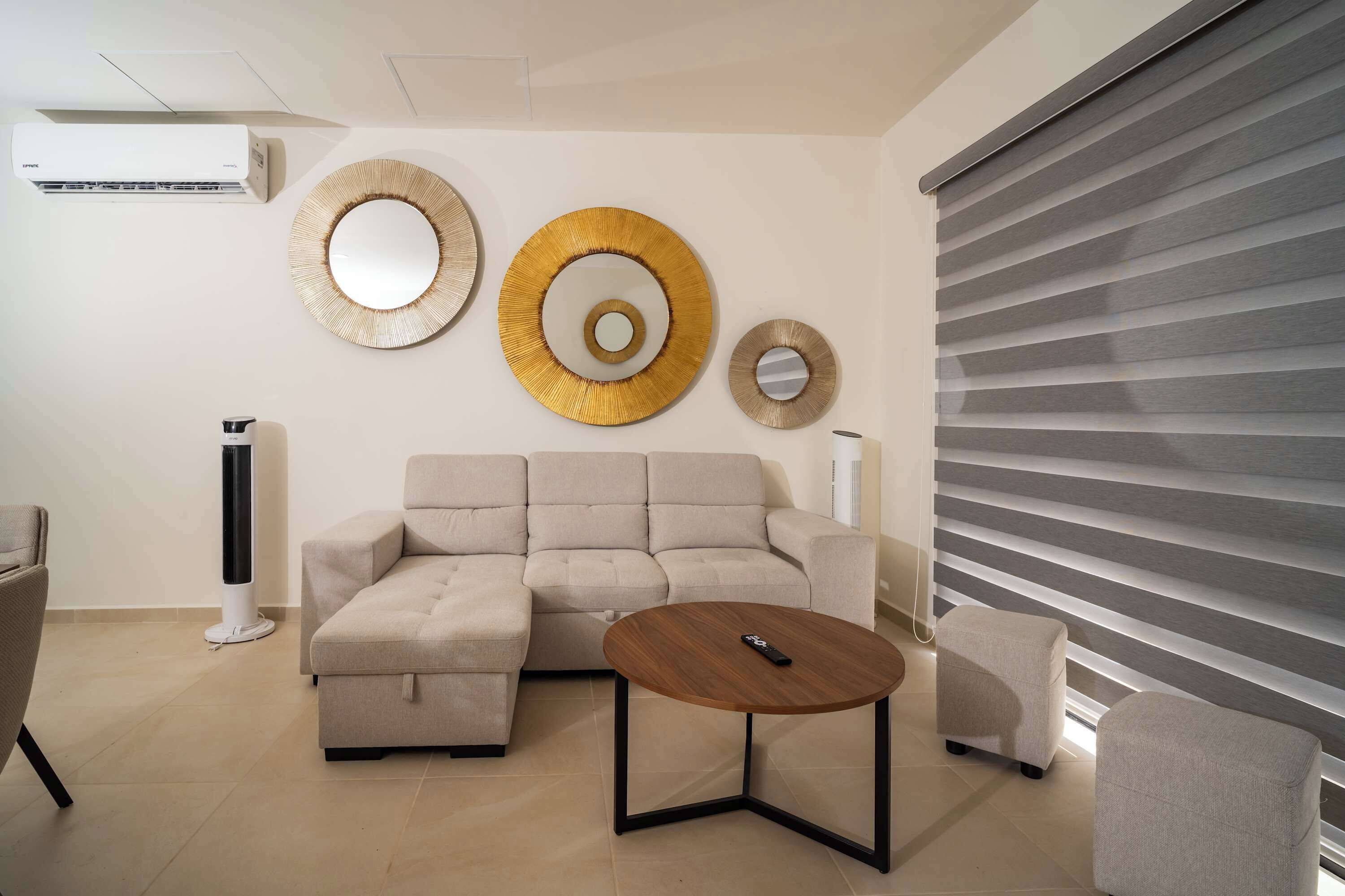 Una sala moderna con un sofá seccional color beige, una mesa de centro redonda de madera y un calentador de pie.
