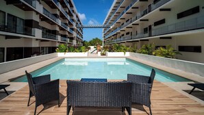 A modern hotel pool area with a clear view of the pool, surrounded by black wicker furniture and a tiled deck. - Modern retreat with Rooftop Pool + Work Lounge (Cancún)
