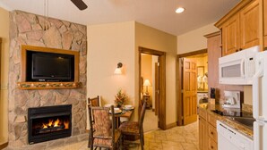 Una cocina con chimenea de piedra, un comedor con sillas, un televisor montado en la pared y armarios de madera.