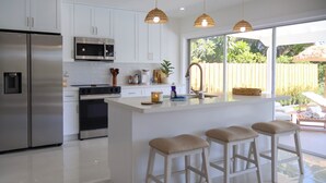 Een moderne keuken met roestvrijstalen apparatuur, een groot kookeiland met barstoelen en uitzicht op de achtertuin door een schuifdeur van glas.