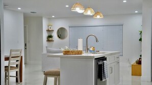 Een moderne keuken met een centraal eiland, inbouwapparatuur en hangende lampen.
