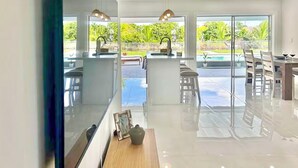 Een moderne keuken met een groot eiland, een eetgedeelte met uitzicht op het zwembad, en een ruime woonkamer met grote ramen.