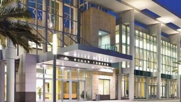 A modern hotel entrance with a glass facade, a prominent sign reading "Ocean Center," and a palm tree to the left. - Wonderful Apartment on the Beach (Daytona Beach)