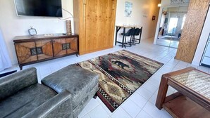 A living room with a sofa, a TV mounted on the wall, a wooden cabinet, and a patterned rug. - Wonderful Apartment on the Beach (Daytona Beach)