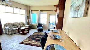 A spacious living room with a sofa, a coffee table, and a dining table set for two. - Wonderful Apartment on the Beach (Daytona Beach)
