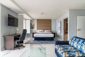 Une chambre moderne avec un lit, un bureau, une chaise, un canapé et un téléviseur fixé au mur.