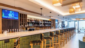 A modern bar area with a TV displaying a sports event, a variety of bottles, and a seating arrangement with unique chairs. - Lagoon Shoreline Penthouse (Cape Town)