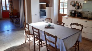 A dining area with a table and chairs, a kitchen with appliances, and a view of the outdoors. - An eco-renovated house full of charm, a garden and a magnificent view. (Varen)