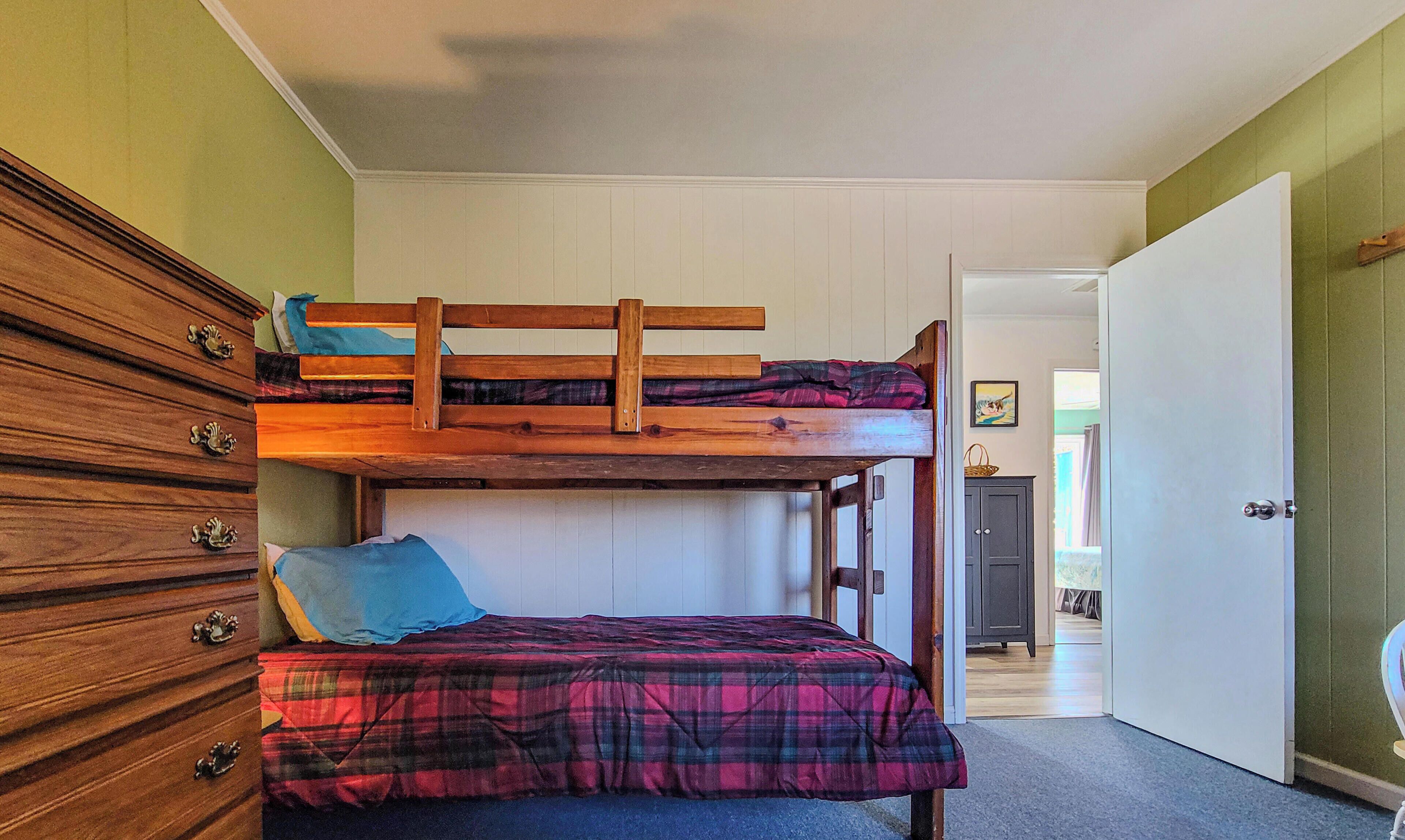 Een stapelbed met een houten hoofdbord, een dressoir met meerdere lades en een vloerbedekking.