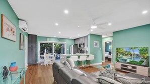 A modern living room with a grey sofa, a glass coffee table, and a flat-screen TV. - NEW Tropical Oasis with Heated Pool & Tiki Hut (Pompano Beach)