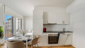 Una cocina compacta con armarios blancos, encimera negra y horno empotrado.