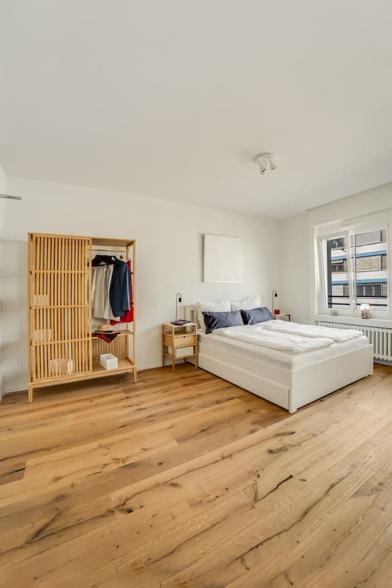 A bedroom with a wooden floor, a bed, a wardrobe, and a window.