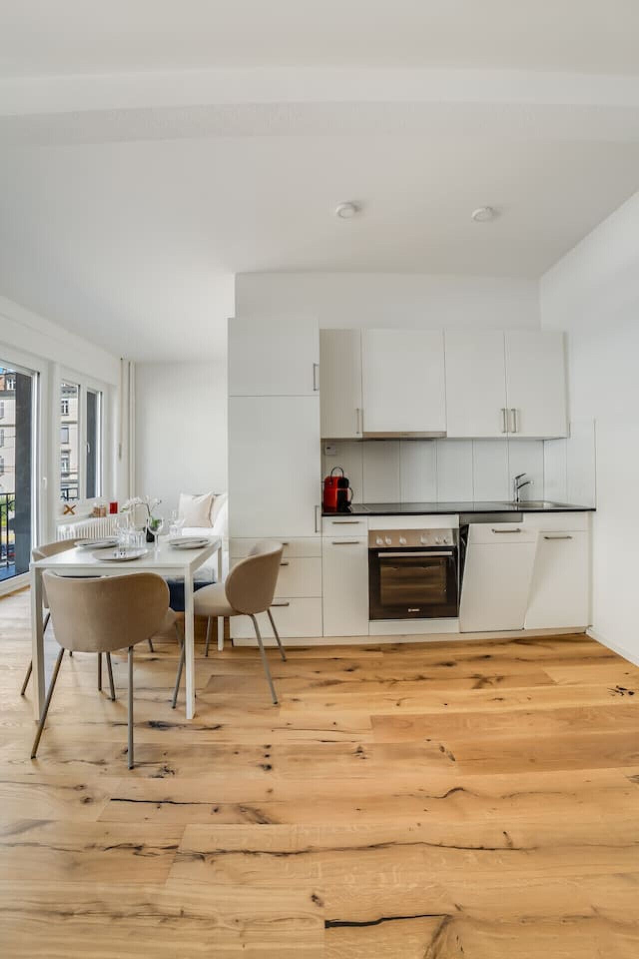 Une cuisine moderne avec des meubles blancs, une cuisinière noire et un coin repas comprenant une table et des chaises.