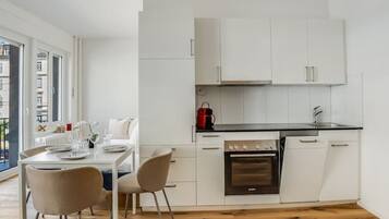 Une cuisine moderne avec des meubles blancs, une cuisinière noire et un coin repas comprenant une table et des chaises.