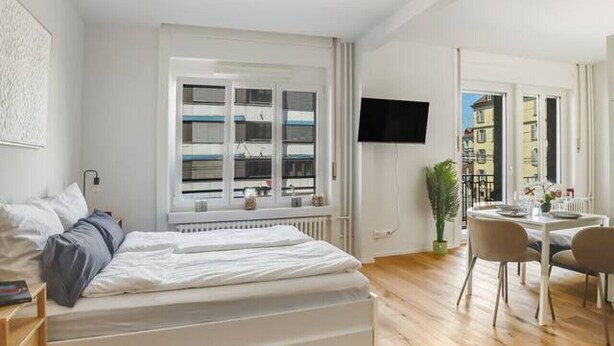 A modern bedroom with a large bed, a desk, and a dining area. - Stylish studio apartment near the Olma trade fair (St. Gallen)