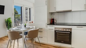 A modern kitchen with white cabinets, a black countertop, and a built-in oven. There is a dining table with chairs and a potted plant. - Stylish studio apartment near the Olma trade fair (St. Gallen)