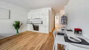 Una cocina moderna con gabinetes blancos, horno empotrado y un comedor con una mesa dispuesta para dos personas.