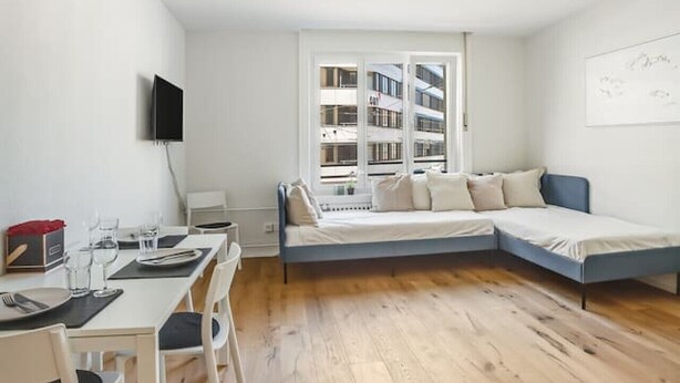 Una sala de estar moderna con comedor, un sofá y un televisor montado en la pared.