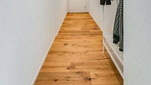 Un pasillo estrecho con paredes blancas y suelo de madera, que conduce a una puerta blanca al final.
