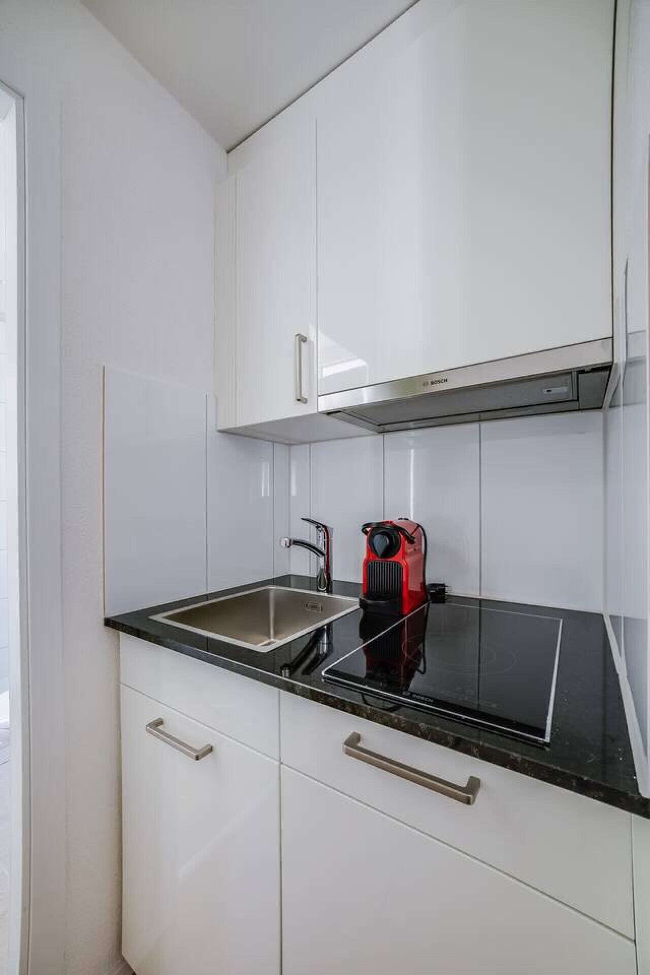Een moderne keuken met witte kastjes, een zwart aanrecht en een rode inbouwtoestel.