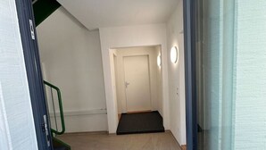 Una vista attraverso una porta che si apre su una stanza con pavimento in legno, una porta e un piccolo gradino che conduce a una scala.