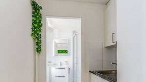 Un corridoio stretto con pavimento in legno che conduce a una zona cucina con mobili bianchi e lavello in acciaio inossidabile.
