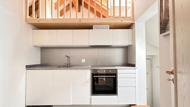 A compact kitchen with white cabinets, a built-in oven, and a wooden ceiling structure. - Cozy 2.5 room apartment in Winterthur (Winterthur)