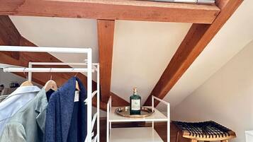 Ein Schlafzimmer im Loft-Stil mit Dachfenster, Holzbalken, einer weißen Regalkonstruktion, einem kleinen Hocker und einer Kleiderstange.