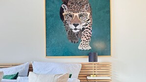 A bedroom with a bed, pillows, a blanket, a painting of a leopard, a bedside table, and a lamp. - Cozy 2.5 room apartment in Winterthur (Winterthur)