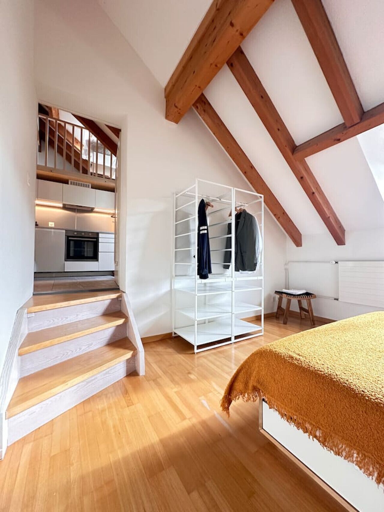 A spacious room with a wooden staircase, a white wardrobe, and a bed with a brown blanket.