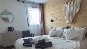 Quarto com cabeceira de madeira, espelho redondo, mesa de cabeceira, cadeira e cama com travesseiros e toalhas.