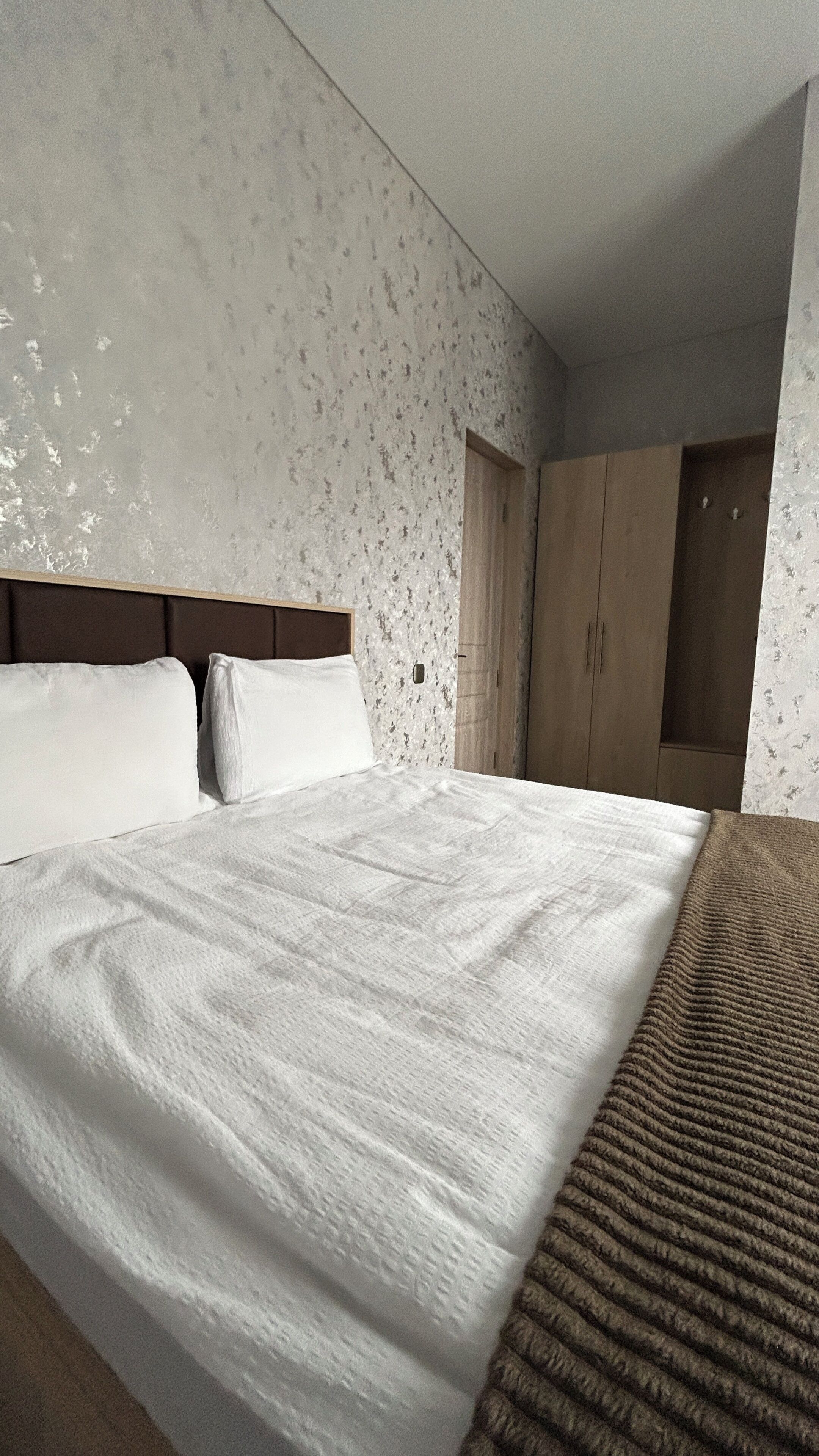 Een moderne hotelkamer met een groot bed, een houten hoofdbord, een kledingkast en een behang met een patroon.