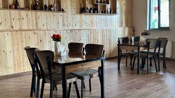 A wooden-paneled room with a dining table and chairs, a chandelier, and shelves with bottles and pottery.