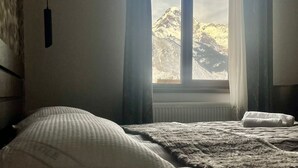 Een slaapkamer met een bed, een raam met gordijnen en uitzicht op een berg.