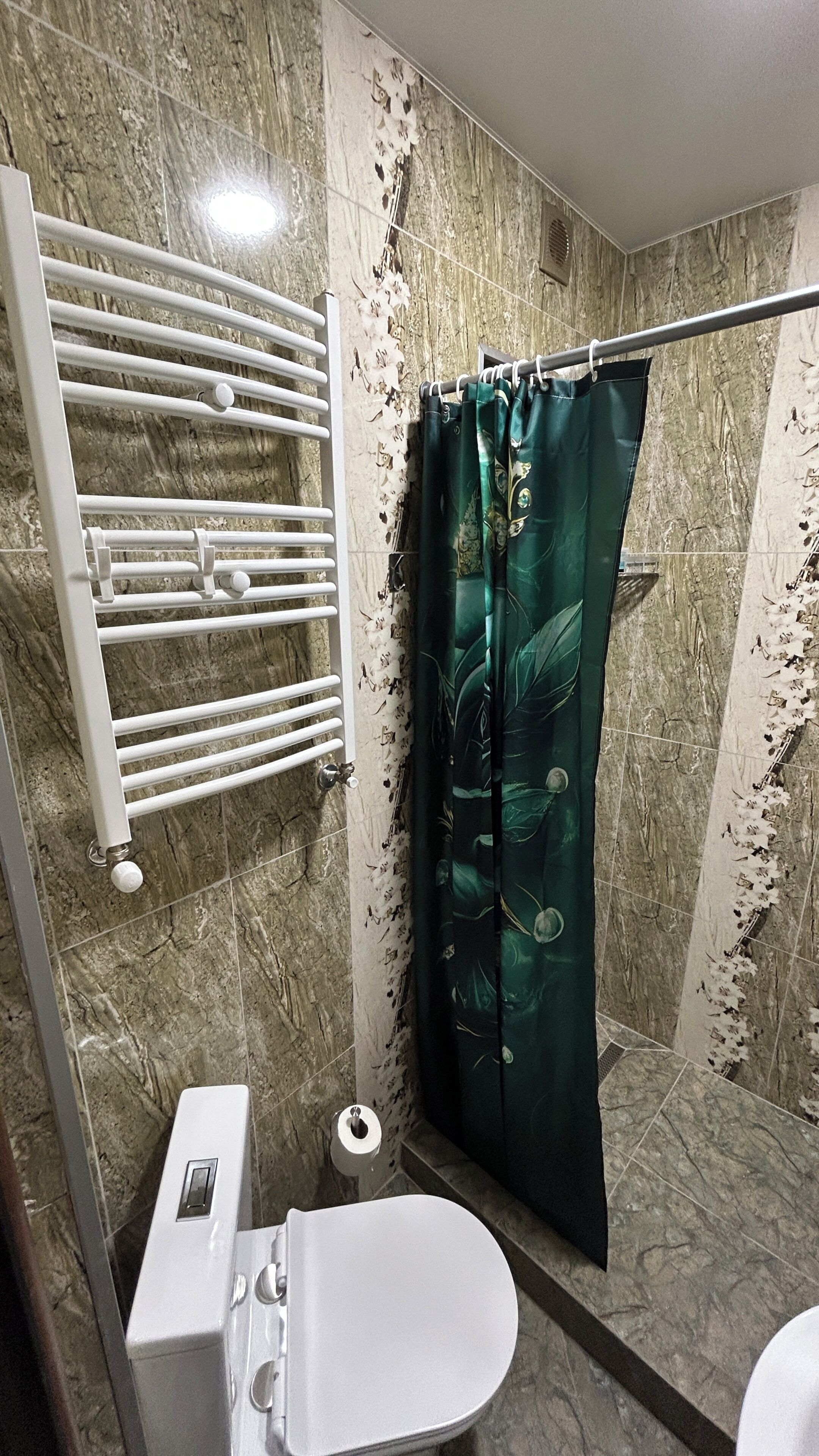 A bathroom with a toilet, a shower curtain, a towel rack, and a marble wall.