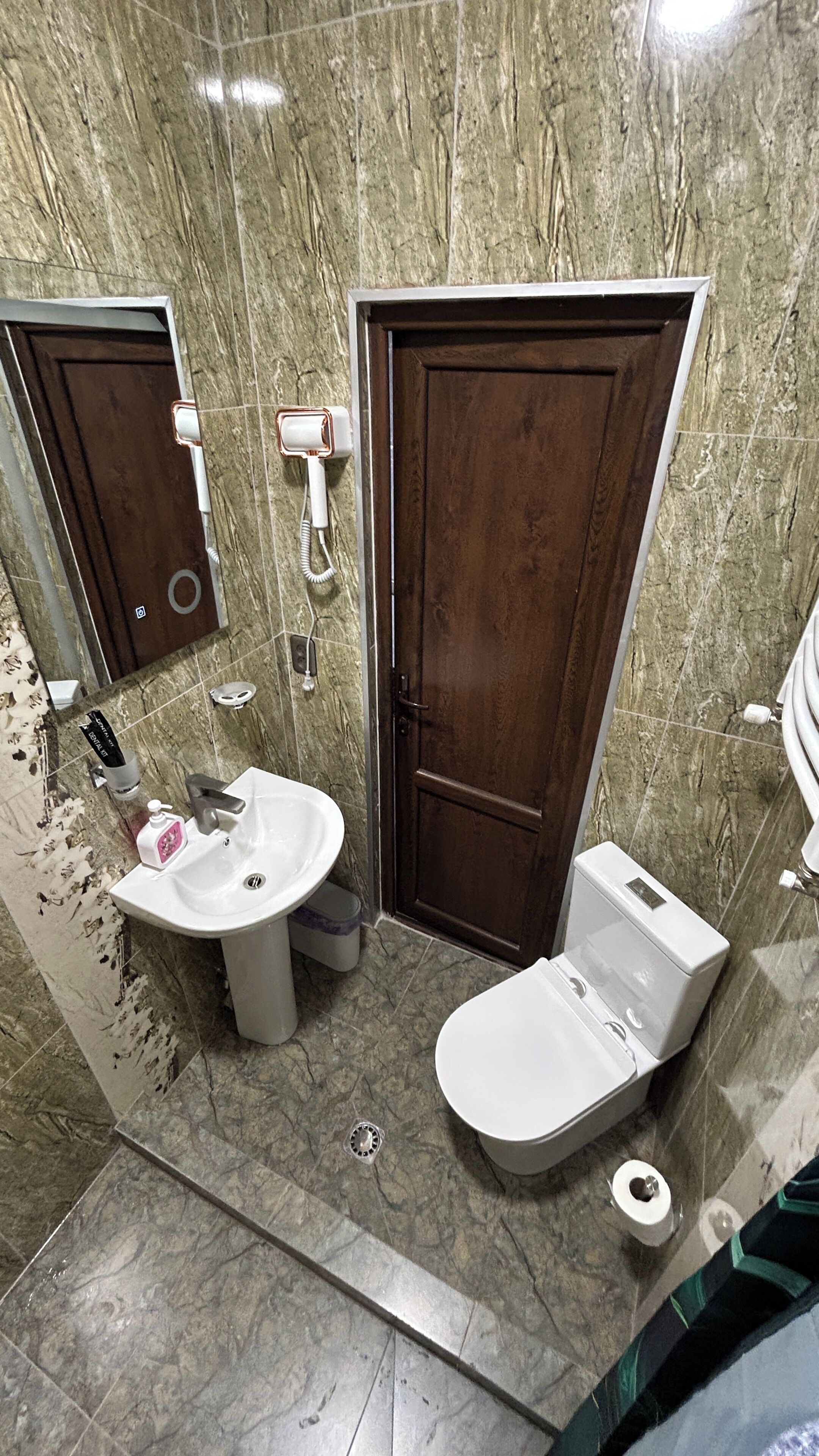 Een badkamer met een marmeren wand, een wastafel, toilet en douche.