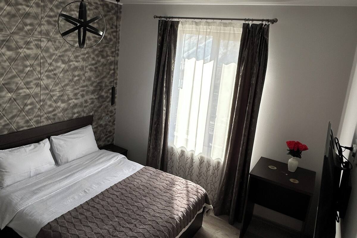 Ein modernes Hotelzimmer mit einem großen Bett, einem Schreibtisch mit Stuhl, einem Fernseher und einem Fenster mit Vorhängen.