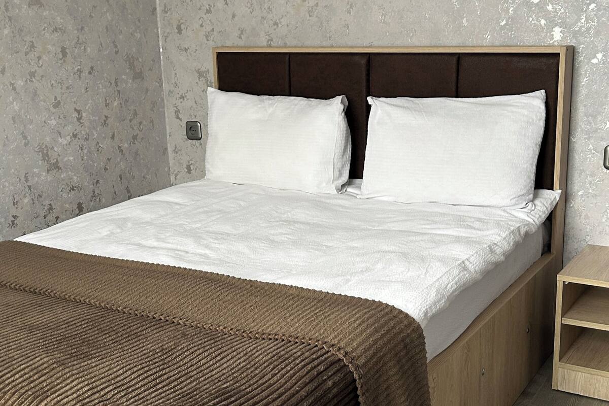 Ein Bett mit Holzrahmen, weißer Bettwäsche und einer braunen Tagesdecke.