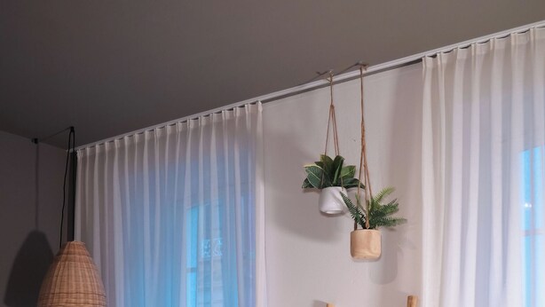 Une chambre avec un lit, des rideaux légers, une plante suspendue, une échelle en bois et un luminaire en fibres tressées.