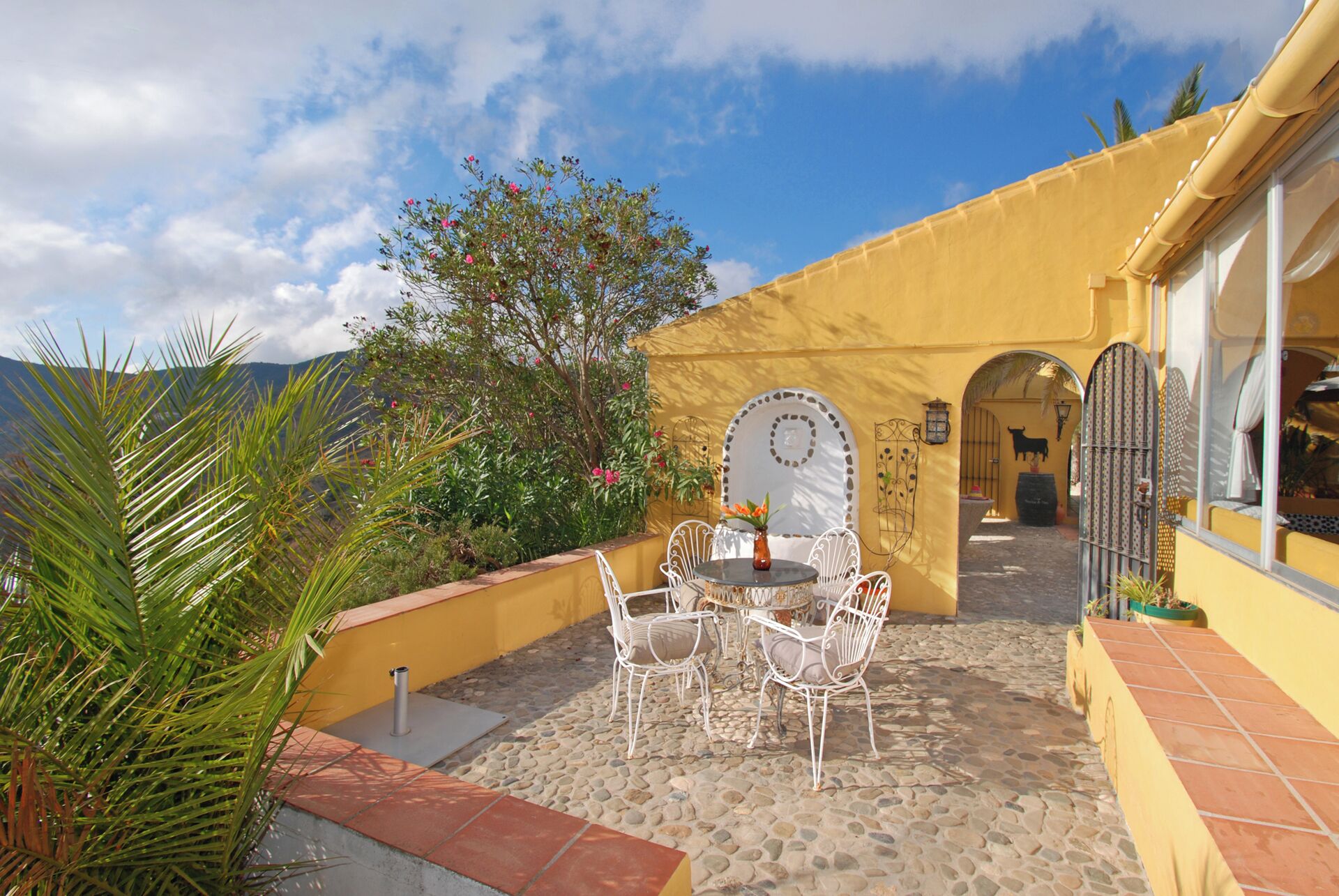 Une terrasse extérieure avec une table et des chaises, un mur jaune et une vue sur les montagnes.