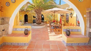 Een terras buiten met een palmboom, houten meubels en betegelde vloer.