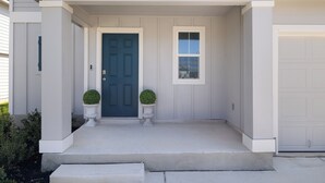 Una casa amb un porxo, una porta blau fosc i dues plantes en testos.