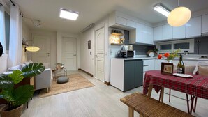 A modern kitchen with white cabinets, a dining area with a red checkered tablecloth, and a cozy seating arrangement. - House Lotus (Seoul)