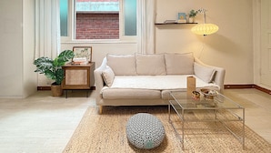 A living room with a sofa, a coffee table, a lamp, a plant, and a bookshelf. - House Lotus (Seoul)