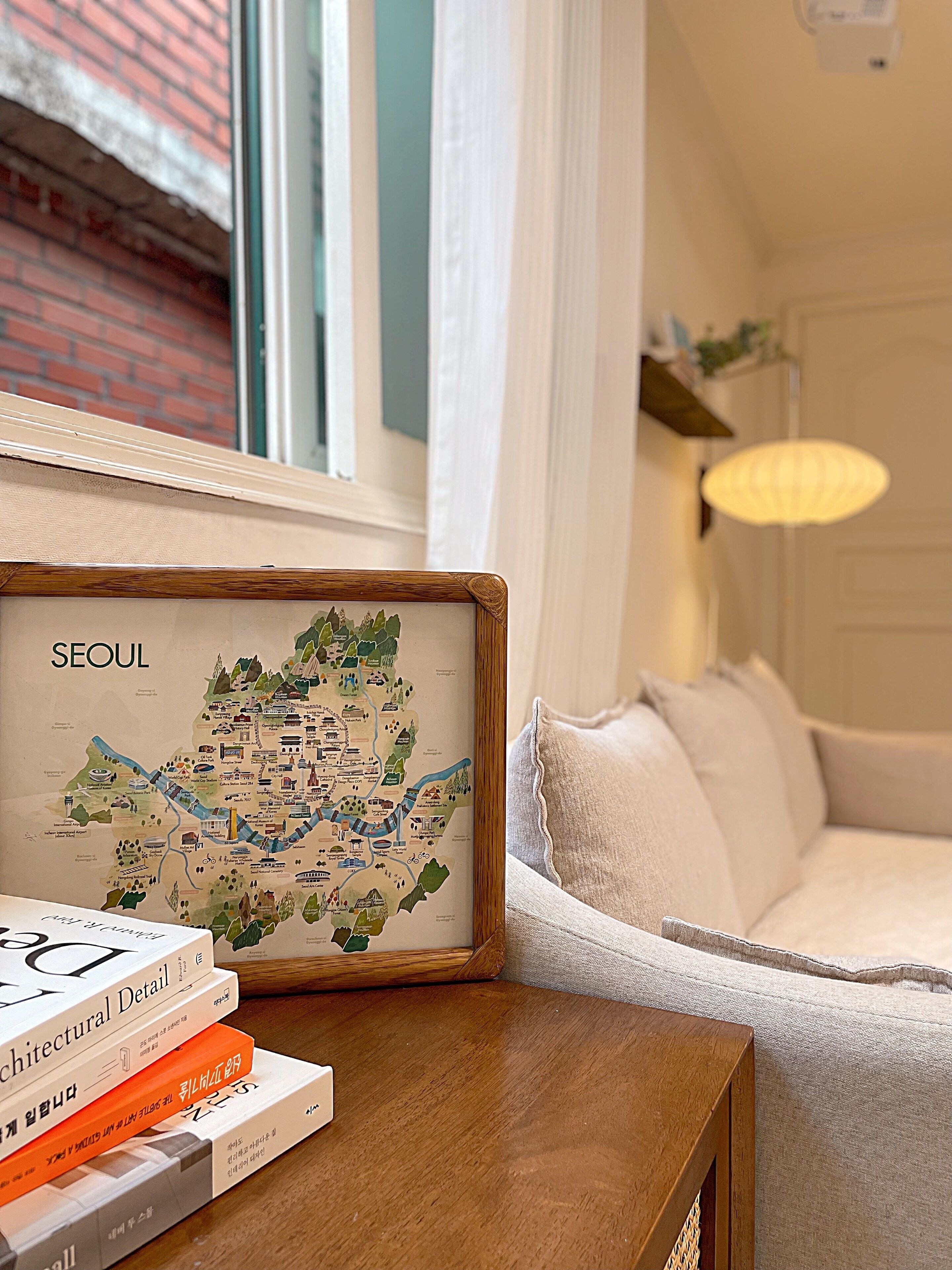 Een ingelijste kaart van Seoul op een houten tafel, naast een bank en een lamp.